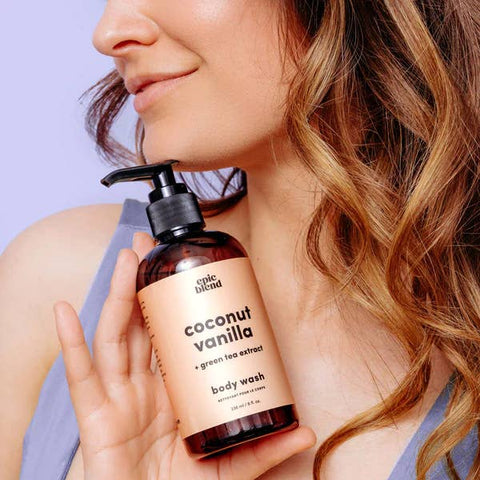 Person holding a bottle of coconut vanilla body wash with a purple background