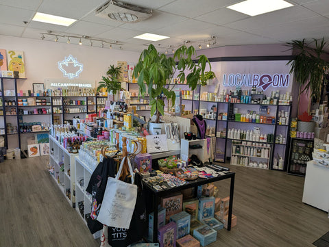 The Local Boom interior with shelves of skincare and beauty products, a central display table with assorted items, potted green plants, and a visible 'LOCAL BOOM' wall sign. 